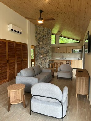 A modern living room with a stone accent wall, wooden ceiling, and a kitchen area with a stone backsplash.