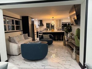 A modern living room with a sofa, armchair, and coffee table, a kitchen with a stove and sink, and a dining area with a bar. - Cafe Estate (Hollywood)