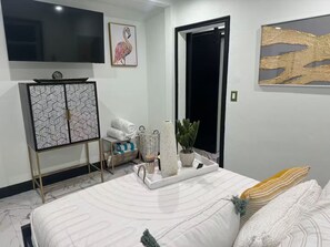 Ein Schlafzimmer mit einem Bett, einem Fernseher, einer Tür und einer Wand mit einem Gemälde.