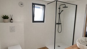 Un baño moderno con cabina de ducha de vidrio, inodoro, ventana pequeña y lavamanos de mármol.