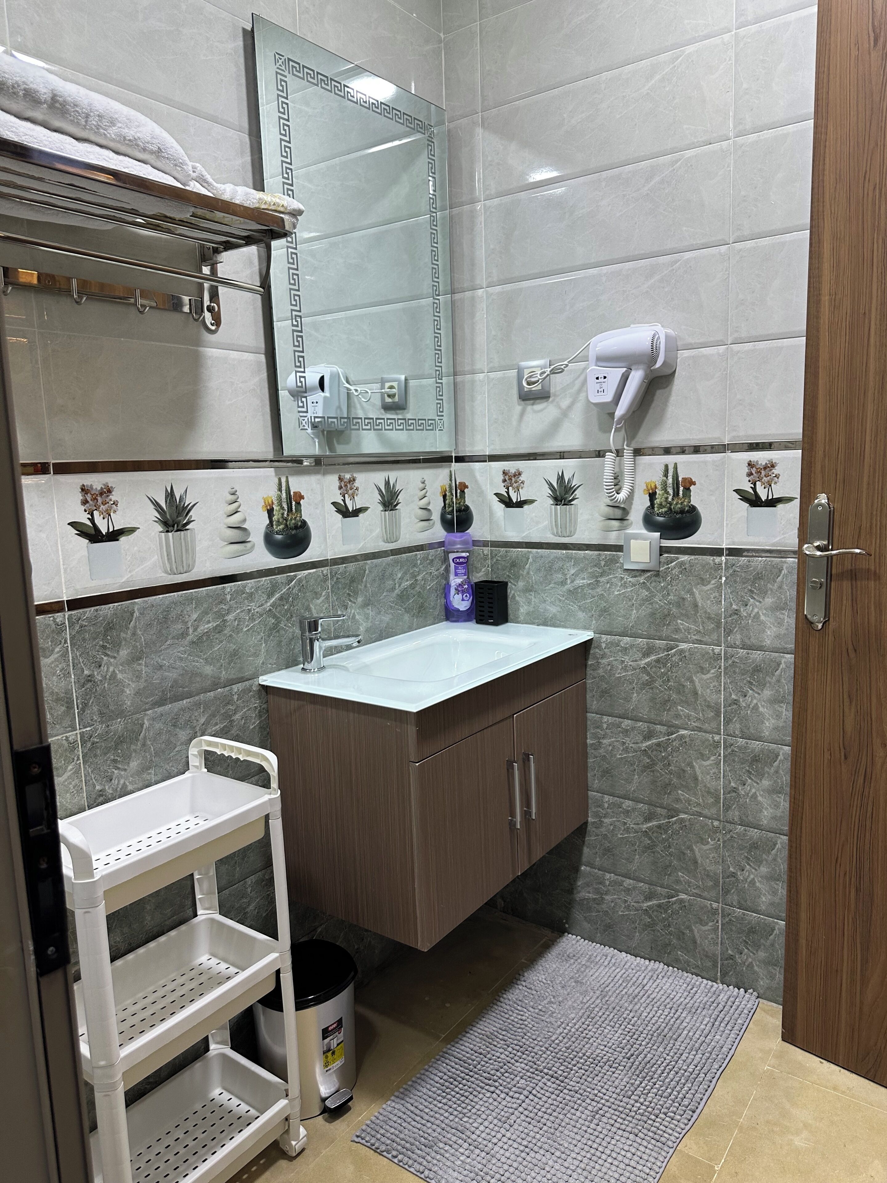 Casa de banho com lavatório, espelho, porta-toalhas e secador de cabelo.