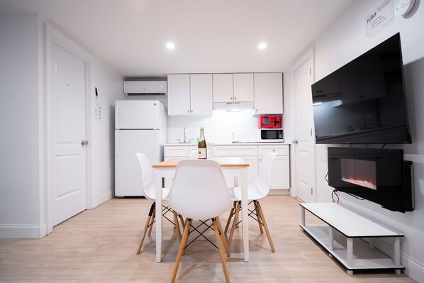 A modern kitchen with white cabinetry, a built-in oven, a microwave, and a flat-screen TV mounted on the wall. - Peaceful 4-bedroom apartment with AC in vibrant Flushing (Flushing)