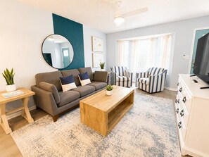 Ein modernes Wohnzimmer mit einer Couch, einem Couchtisch, gestreiften Stühlen, einem Fernseher und einem Spiegel.