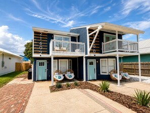 A two-story house with a balcony, a front porch with seating, and a driveway. - Fully Renovated Beach Retreat Townhome Combo! (Panama City Beach)