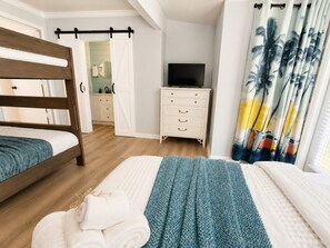 A bedroom with a wooden bed, a white dresser, a television, and a window with curtains. - Fully Renovated Beach Retreat Townhome Combo! (Panama City Beach)