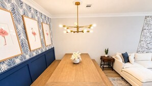Zona pranzo con tavolo di legno, panche, un lampadario, opere d'arte incorniciate e un divano.