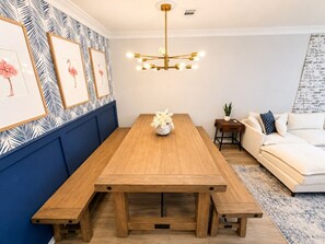 Ein Essbereich mit Holztisch, Bänken, einer Deckenleuchte, gerahmten Kunstwerken und einem Sofa.