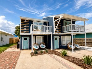 A two-story house with a balcony, a front porch with seating, and a driveway. - Fully Renovated Beach Retreat Townhome Combo! (Panama City Beach)