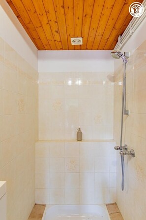 A shower with a wooden ceiling, tiled walls, and a handheld showerhead.