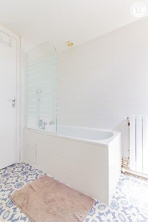 Ein Badezimmer mit Badewanne, einer Duschkabine aus Glas und fliesenbesetztem Boden.