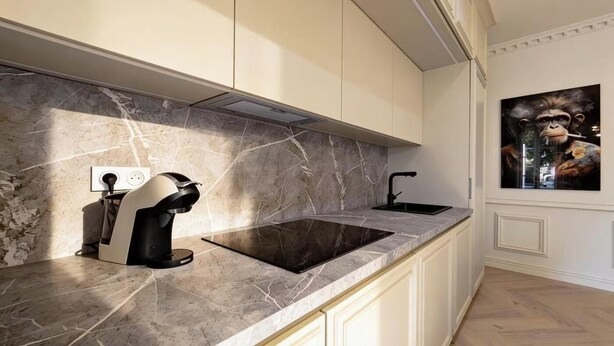 Una cocina moderna con encimera de mármol, estufa empotrada y cafetera de pared.