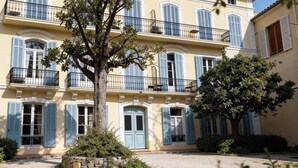 Un edificio de varios pisos con balcones, un árbol en primer plano y un patio de grava.
