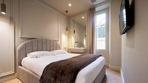 Un dormitorio moderno con una cama grande, una mesita de noche, un espejo y un televisor fijado a la pared.