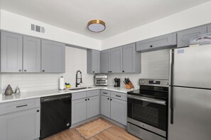 A modern kitchen with grey cabinets, a stainless steel refrigerator, a dishwasher, an oven, and a sink.