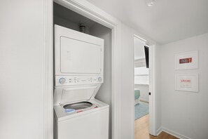 A laundry room with a front-loading washer and dryer, a door leading to another room, and a framed picture on the wall.