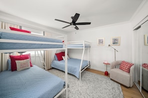 A bunk bed room with a ceiling fan, a small armchair, and a patterned rug.