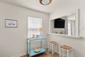 A room with a glass console table, two white stools, a framed picture on the wall, and a window with blinds. - 3-bedroom condo conveniently located near Campus and the Square! (Oxford)
