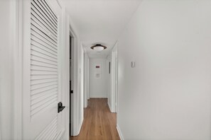 A hallway with white walls, wooden flooring, and a ceiling light fixture. - 3-bedroom condo conveniently located near Campus and the Square! (Oxford)
