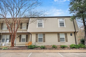A two-story apartment building with a brick facade, multiple windows, and a small porch with a bench. - 3-bedroom condo conveniently located near Campus and the Square! (Oxford)