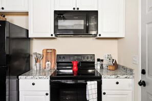 Una cocina con microondas negro, estufa y horno, armarios blancos y encimera de mármol.