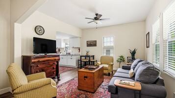 A living room with a sofa, armchair, wooden chest, and a television.