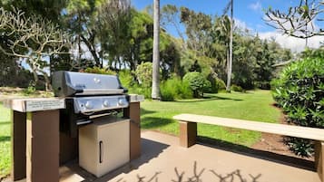 An outdoor grill station with a bench, surrounded by greenery and trees.