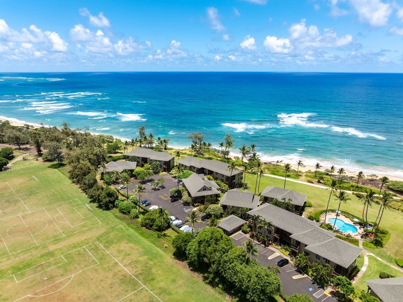 An aerial view of a resort with multiple buildings, a swimming pool, and a beach.