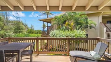 A covered outdoor area with a wooden deck, wicker furniture, and a view of a building with a palm tree.