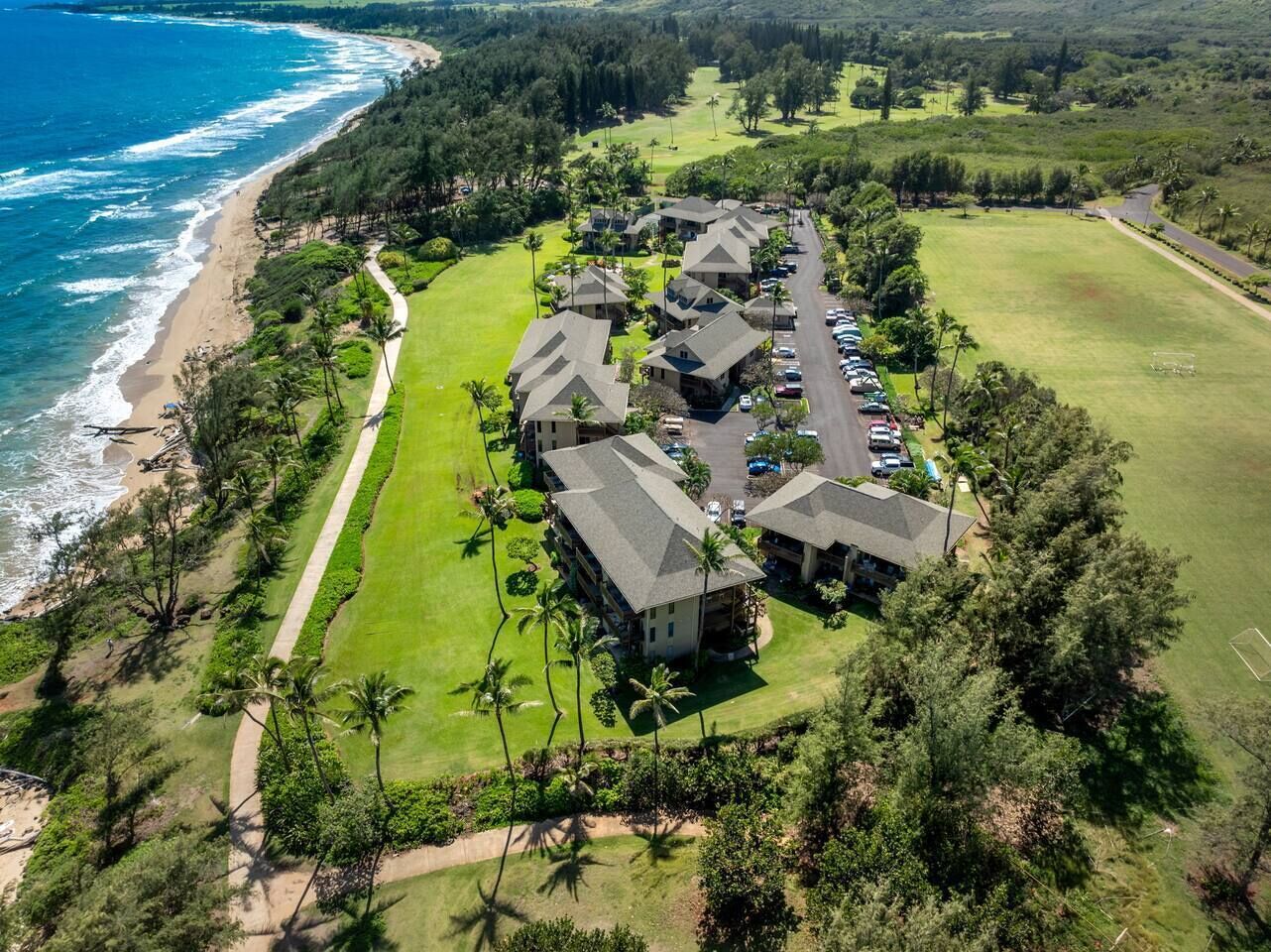 An aerial view of a coastal resort with multiple buildings, a parking lot, and a golf course.