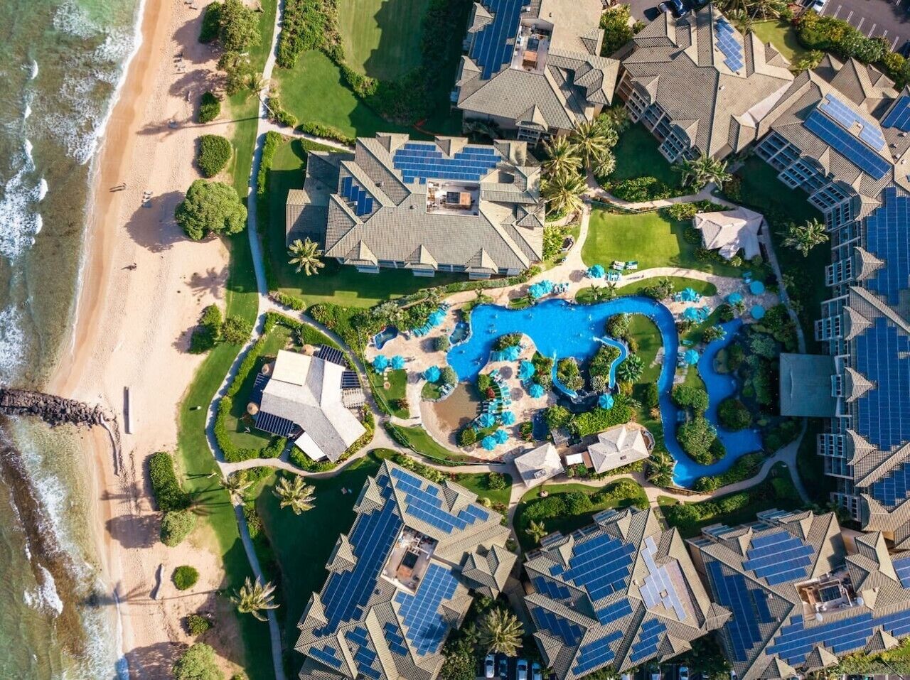 An aerial view of a resort with multiple buildings, a swimming pool, and a beach.