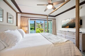 A hotel room with a bed, a ceiling fan, a TV, and a view of a pool and greenery. - Waipouli C102 / 2 King Beds / AC  / Pool (Kapaʻa)