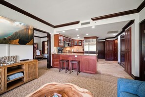 A spacious living area with a wooden entertainment unit, a large wooden coffee table, and a kitchen with a central island and bar stools. - Waipouli C102 / 2 King Beds / AC  / Pool (Kapaʻa)