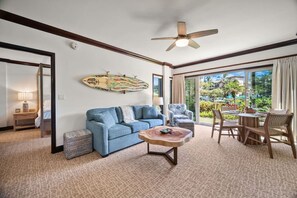 A room with a blue sofa, a wooden coffee table, a ceiling fan, and a dining area with wicker chairs. - Waipouli C102 / 2 King Beds / AC  / Pool (Kapaʻa)