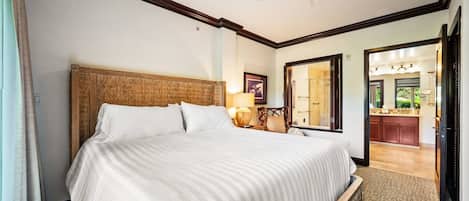 Habitación de hotel con una cama grande, ventilador de techo, mesita de noche con lámpara y vista al baño a través de una puerta abierta.