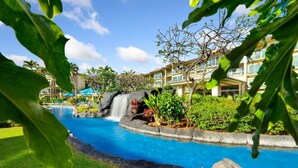 A resort pool with a waterfall feature, surrounded by lush greenery and a multi-story building with balconies. - A/C Luxury Poolside Retreat / Resort fee included (Kapaʻa)