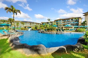 A resort pool with lounge chairs, palm trees, and a multi-story building in the background. - Waipouli C102 / 2 King Beds / AC  / Pool (Kapaʻa)