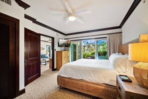 A hotel room with a bed, a television, a ceiling fan, and a view of a tropical landscape. - Waipouli C102 / 2 King Beds / AC  / Pool (Kapaʻa)