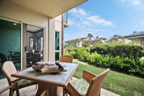 A patio with wicker furniture and a glass table, overlooking a well-maintained garden and a residential area. - Waipouli C102 / 2 King Beds / AC  / Pool (Kapaʻa)