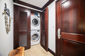 A laundry room with two stacked washing machines, wooden doors, and a stone wall decoration. - Waipouli C102 / 2 King Beds / AC  / Pool (Kapaʻa)