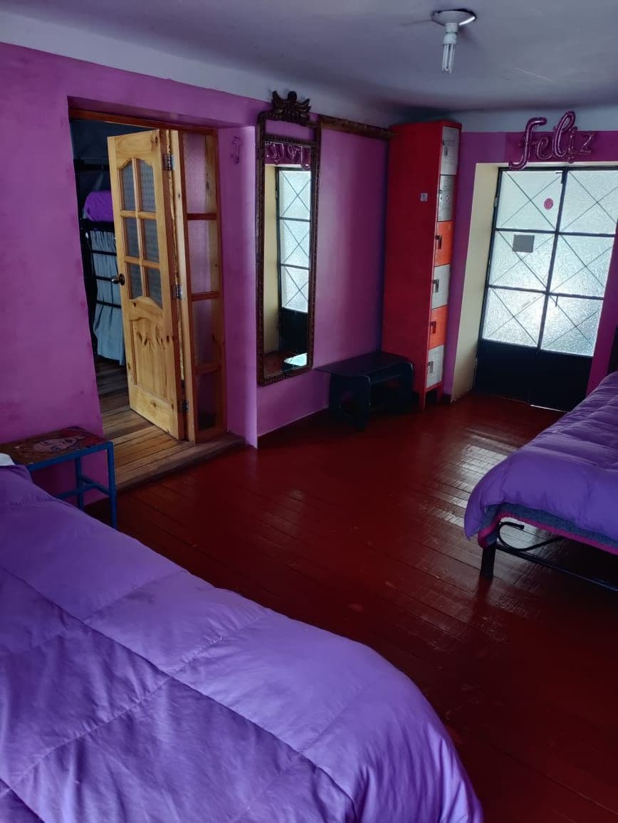 Una habitación con dos camas, una puerta de madera, un espejo, una pared roja y una ventana con vistas.