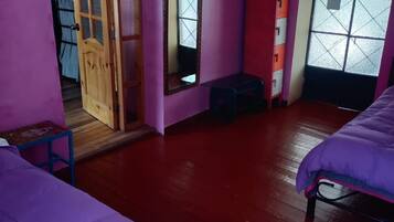 Una habitación con dos camas, una puerta de madera, un espejo, una pared roja y una ventana con vistas.