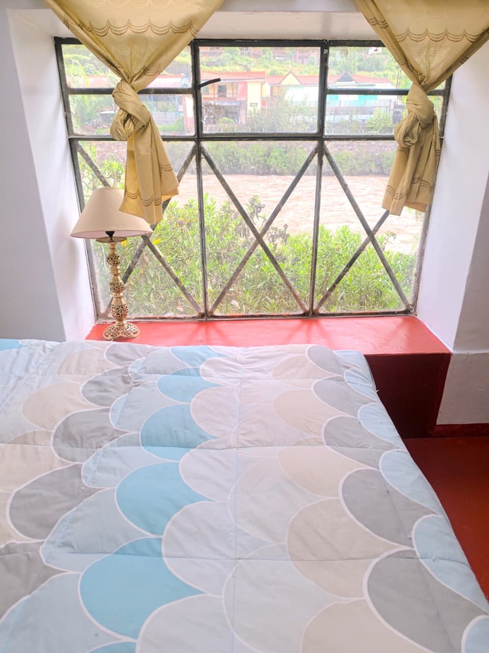A room with a bed, a window with curtains, and a lamp.