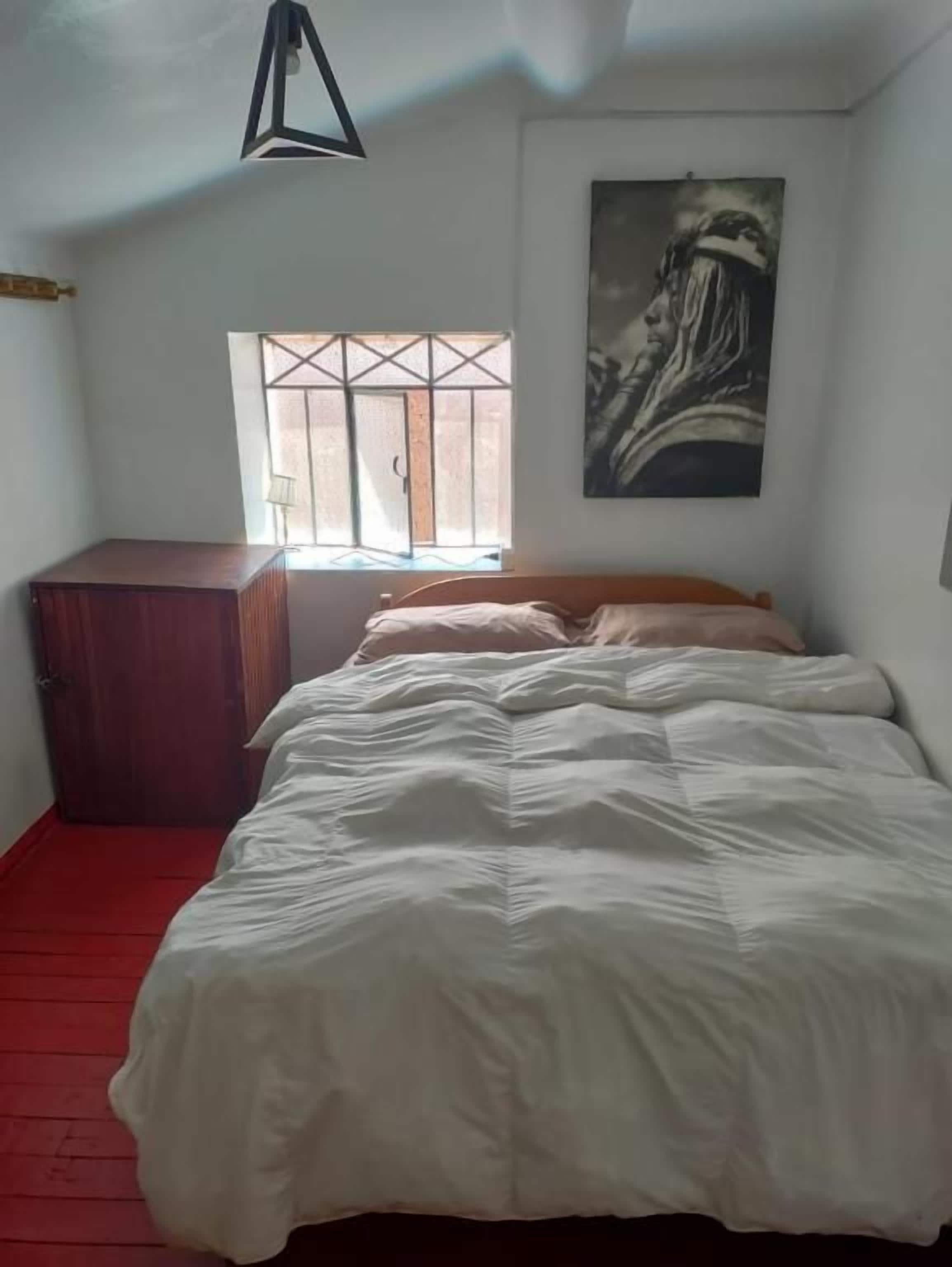 A bedroom with a bed, a window, a painting, and a wardrobe.
