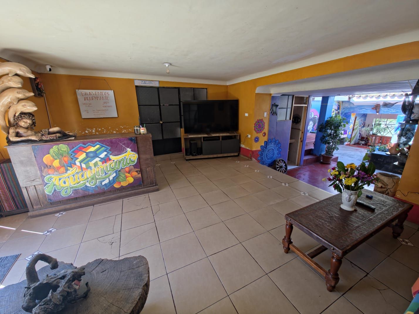 A reception area with a counter, a television, and a dining table with a vase of flowers.