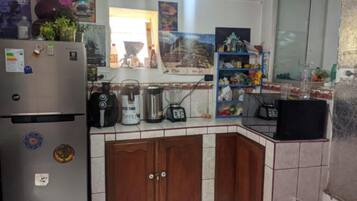 Una cocina con refrigerador, cafetera, licuadora y una repisa con varios objetos.