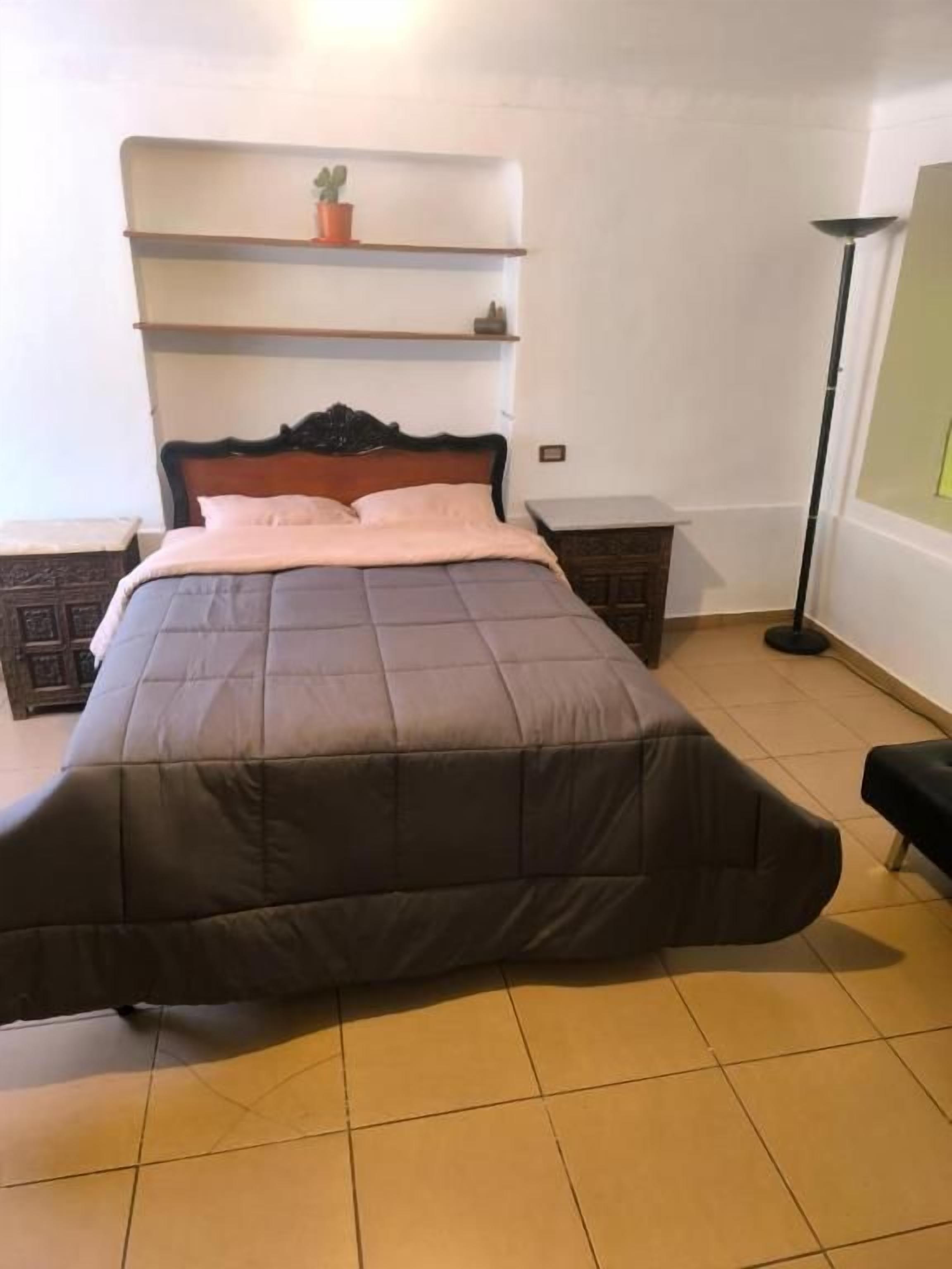 Ein Schlafzimmer mit einem Bett, einem Nachttisch, einer Stehlampe und einem Regal mit einer Topfpflanze.