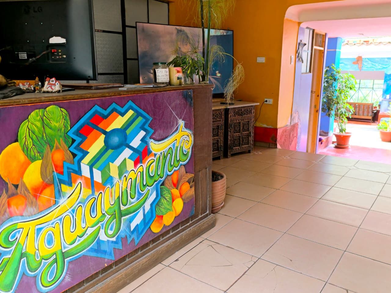 Un comptoir d’accueil aux couleurs vives, agrémenté d’une fresque murale éclatante, un sol carrelé et un aperçu d’une pièce avec un lit et une fenêtre.