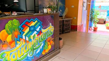 Un comptoir d’accueil aux couleurs vives, agrémenté d’une fresque murale éclatante, un sol carrelé et un aperçu d’une pièce avec un lit et une fenêtre.
