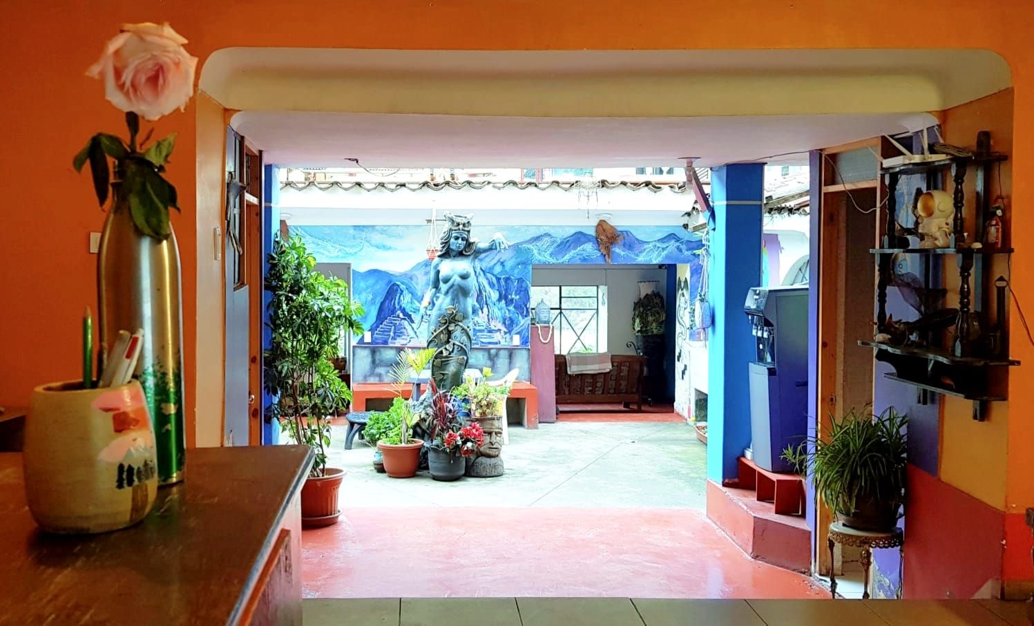 Una habitación con un mural grande, plantas en macetas y una estatua.