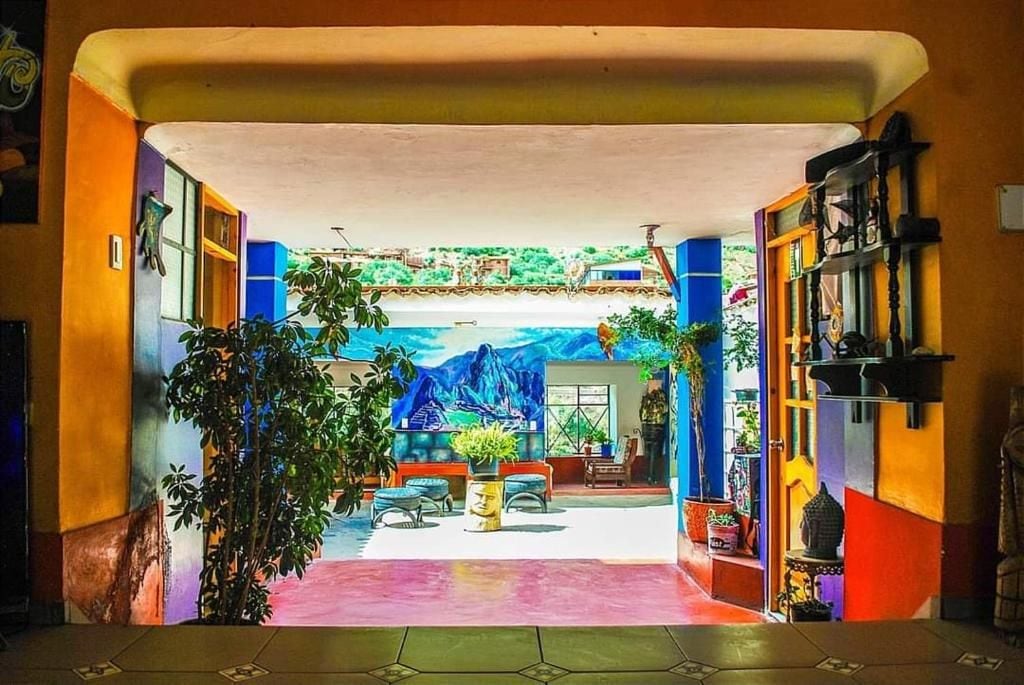 Un intérieur coloré avec un espace salon central, une fresque murale au fond et une variété de plantes.